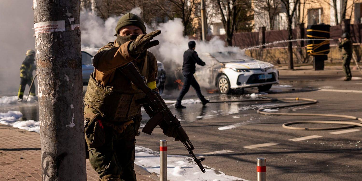Ukrainska soldater på gatan utanför en militäranläggning i Kiev, där två bilar står i brand.